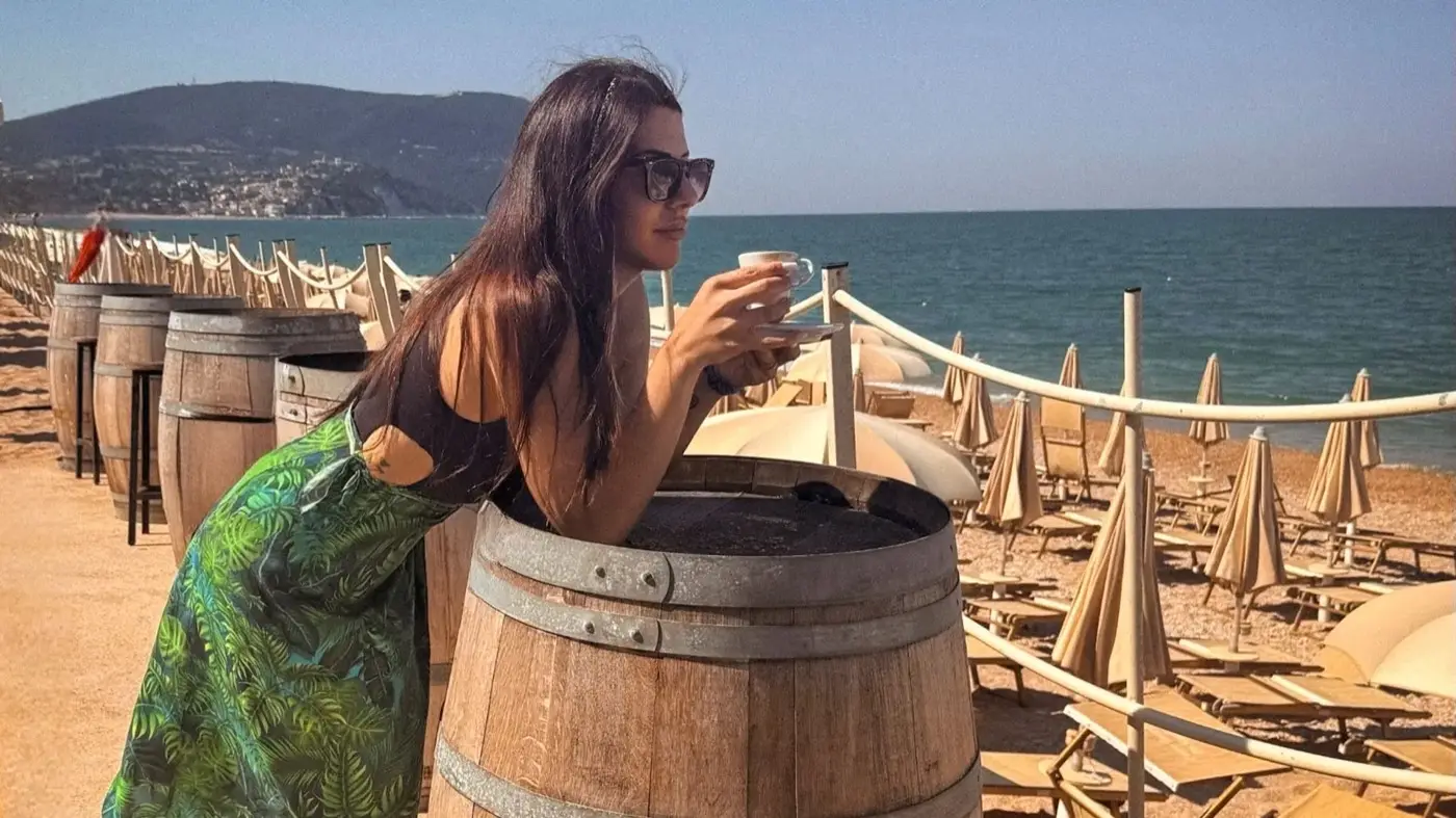 Ospite con un caffè in spiaggia, ombrelloni chiusi e il Monte Conero sullo sfondo