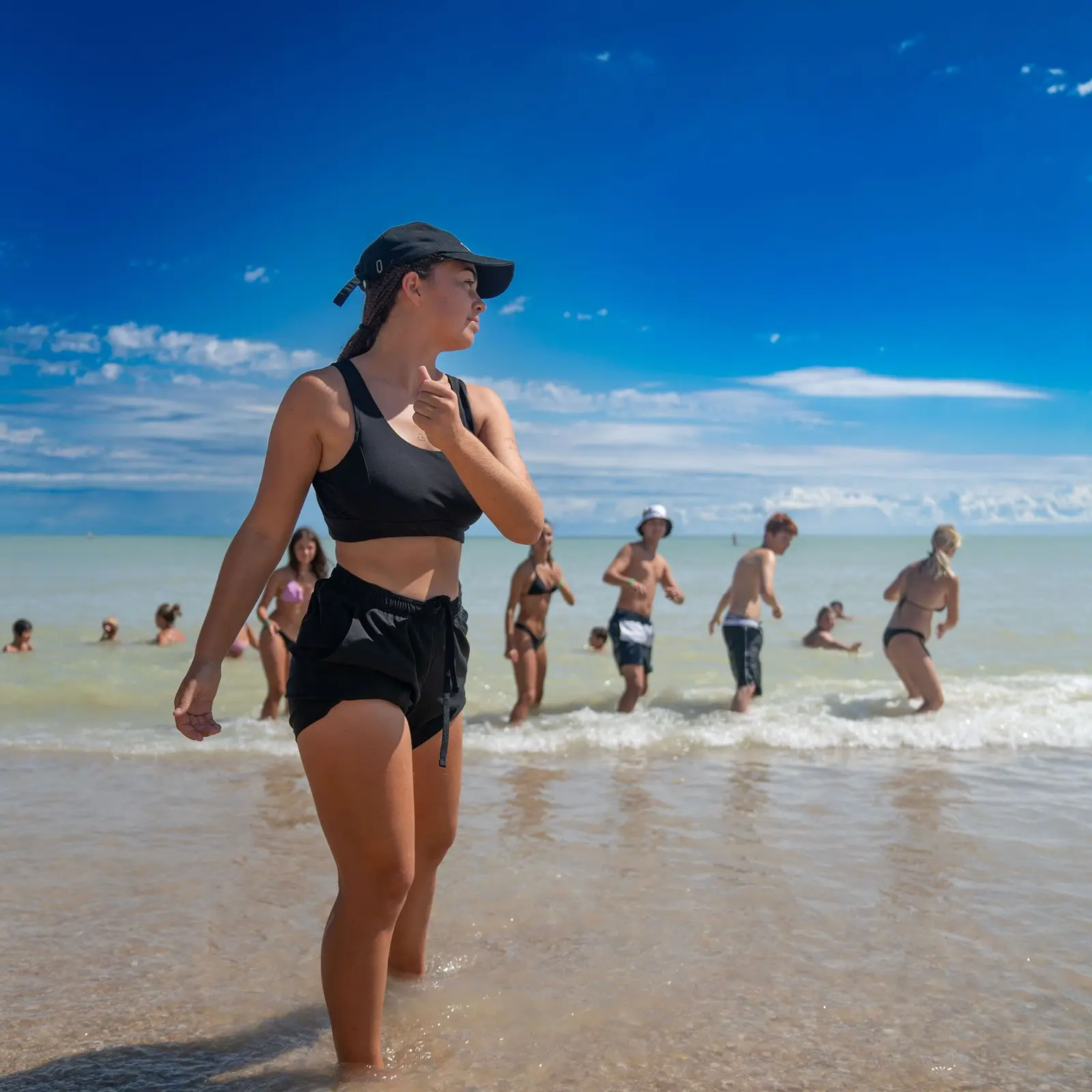 Ragazza in riva al mare con amici che giocano in acqua sotto un cielo blu